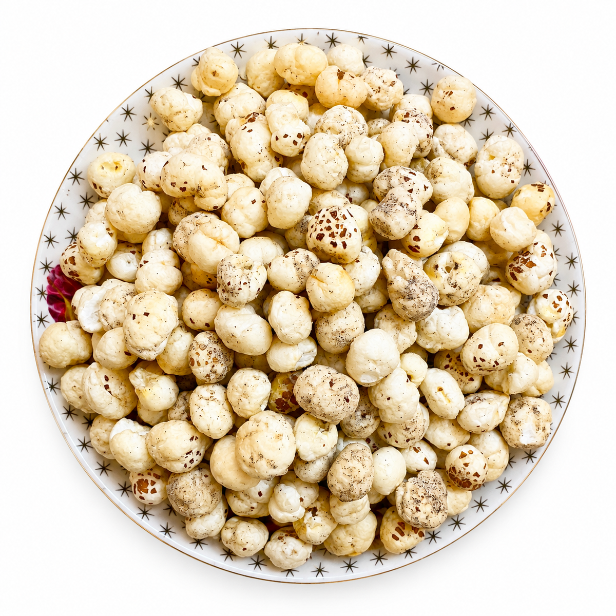 A top-down view of a white ceramic plate with a black star pattern, filled with roasted Himalayan Pink Salt popcorn kernels on a solid white background.